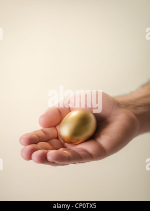 Man showing oeuf d'or et de le tenir en main. Concept de sécurisation de l'épargne, les gens de l'argent, pierres précieuses et choses précieuses, des prix. Banque D'Images