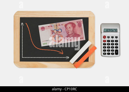 Tableau, graphique avec une courbe a diminué. Sur le tableau se trouve un billet de 100 Yuan chinois avec le portrait de Mao Zedong. Banque D'Images