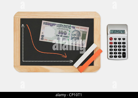 Tableau, graphique avec une courbe a diminué. Sur le tableau se trouve une roupie indienne 100 Projet de loi avec le portrait de Mahatma Gandhi. Banque D'Images
