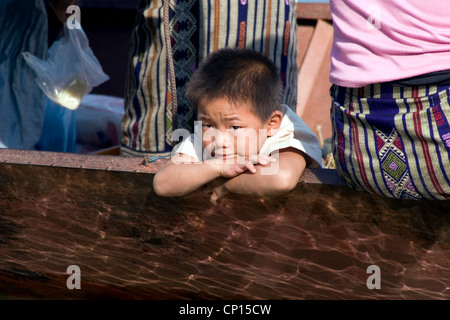 Un jeune garçon asiatique vivant dans la pauvreté est au repos dans un bateau de pêche longtail sur le Mékong à Luang Prabang, Laos. Banque D'Images