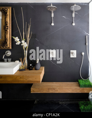 Salle de bains avec mur gris foncé, orné miroir dans cadre doré, double lavabo et douche avec banquette Banque D'Images