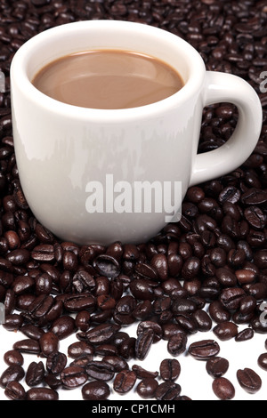 Photo d'une tasse en céramique pleine de café chaud entouré d'un mélange de grains de café arabica et robusta. Banque D'Images