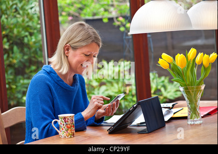 Femme blonde travailler à domicile dans son jardin d'hiver à l'aide de l'ordinateur tablette iPad Apple et des sms sur son smartphone iPhone 4s Banque D'Images