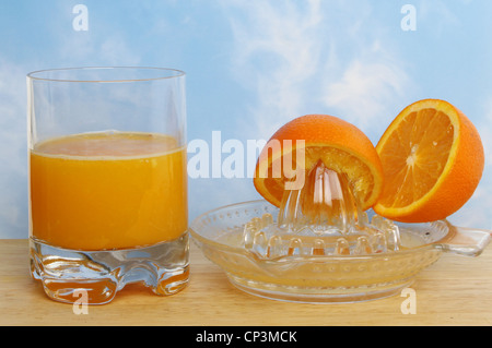 Le jus d'orange fraîchement pressé dans un verre avec une centrifugeuse et oranges sur un conseil sur un fond de ciel bleu Banque D'Images