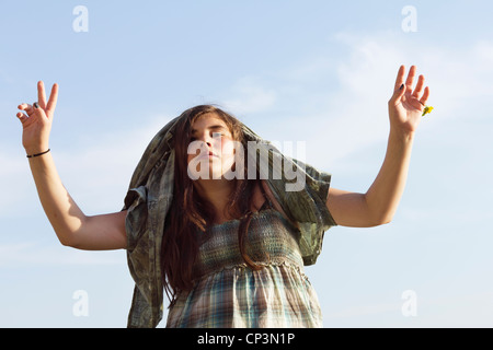 S'amuser - young woman with hands up ayant une chemise par dessus sa tête. Plein air drôle tourné contre un ciel bleu. Banque D'Images