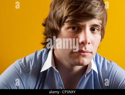 Headshot couleur de modèle masculin wearing blue shirt photographié contre toile jaune Banque D'Images