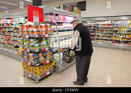 Vieil homme shopping du lait dans un supermarché à la fin de l'allée des produits laitiers. Banque D'Images