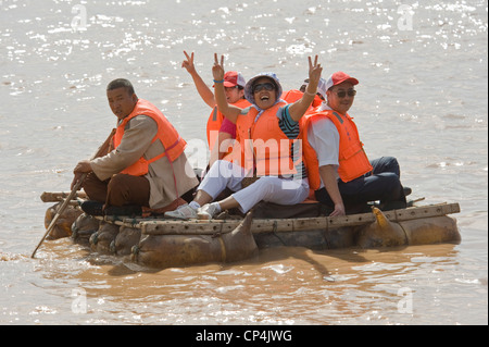 Heureux les touristes chinois flottent sur le fleuve Jaune sur des radeaux en peau de mouton - l'une des "rides" au parc à thème Shapatou. Banque D'Images