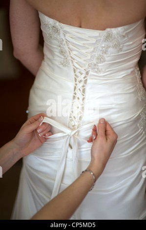 Liage de demoiselle l'archet sur une robe de mariage de la mariée le jour de son mariage Banque D'Images