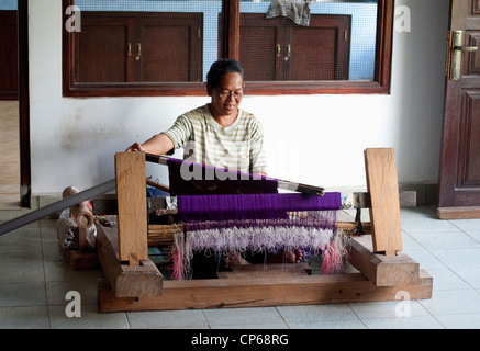 Une femme tisse songket Balinais, un type de tissu qui a un or/ou silver threads qui traverse la pièce sur un métier à tisser à la main. Banque D'Images