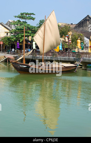 Vue verticale d'un bateau de pêche vietnamien traditionnel avec son voile jusqu'au mouillage près du pont de la rivière Thu Bồn basculant à Hoi An. Banque D'Images