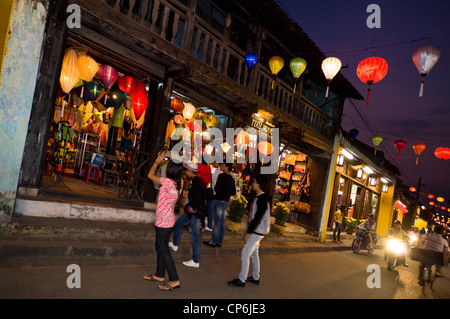 Vue horizontale de touristes prenaient des photos de la lanterne traditionnelle boutiques le long d'une route dans la région de Hoi An décoré avec des lanternes illuminées, au Vietnam. Banque D'Images