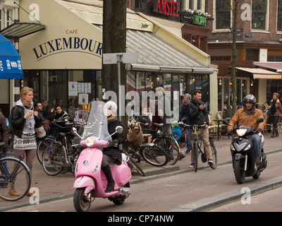 Café Luxembourg à Amsterdam, Pays-Bas avec beaucoup de gens dans la rue et deux scooters qui passent. Banque D'Images