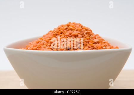 Les lentilles rouges séchés dans un bol blanc sur planche de bois sur un fond blanc. Banque D'Images