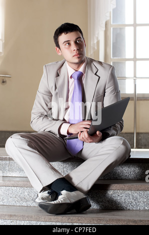 Young businessman sitting on l'escalier avec un ordinateur portable dans les mains Banque D'Images