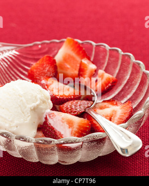 Plat en verre avec des tranches de fraises contre une nappe rouge avec icecream Banque D'Images