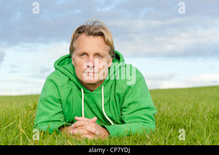 Un portrait d'un homme mûr à la rêveuse aux cheveux blonds portant sur l'herbe et portant un haut vert. Banque D'Images