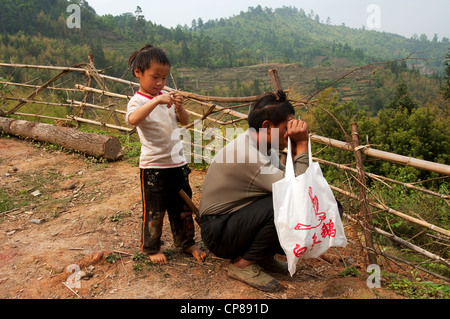 Un basha (Miao) hommes jeune garçon et un homme adulte de remettre un sac shopping avec coiffure traditionnelle, le sud de la Chine Banque D'Images