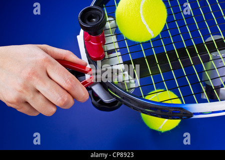 Main tenant une pince tout en chaîne de fraisage sur raquette de tennis sur fond bleu Banque D'Images