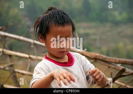 Un basha (Miao) hommes jeune garçon avec la coiffure traditionnelle jouant avec une chaîne, le sud de la Chine Banque D'Images