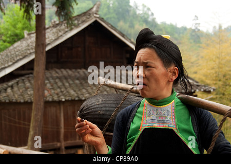 Un basha (Miao) Hommes Femme transportant des marchandises sur ses épaules avec une pièce dans sa main, le sud de la Chine Banque D'Images