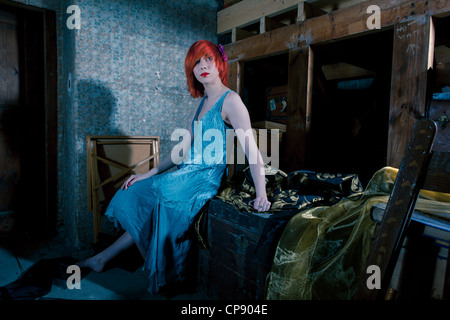 Une belle jeune femme portant une robe de soie bleu assis seul dans un grenier Banque D'Images