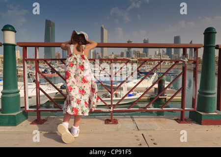 Une jeune fille se repose sur les grilles et les vues du port de plaisance et le Koweït City skyline de Souq Sharq Banque D'Images