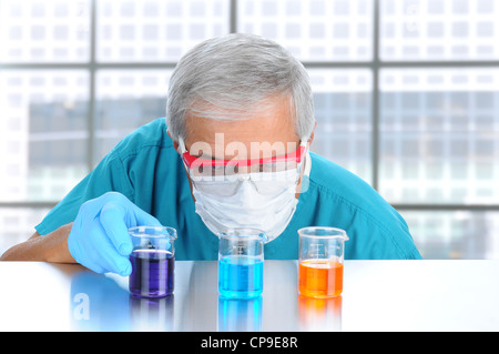 Scientifique dans un laboratoire moderne avec masque de protection et des lunettes de laboratoire l'examen de béchers remplis de produits chimiques différents. Banque D'Images