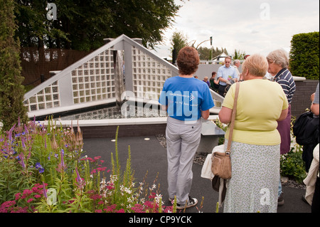Personnes debout avec bénévole, l'affichage en fonction de l'eau jardin Shine for Cancer Research UK - RHS Flower Show, Tatton Park, Cheshire, Angleterre. Banque D'Images