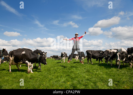 Heureux jeune agriculteur sautant dans domaine avec des vaches Banque D'Images