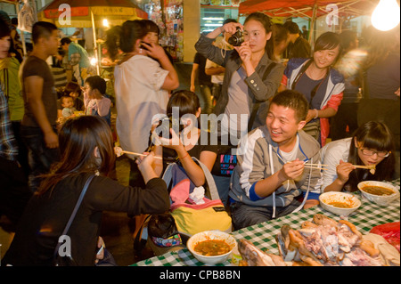 Un groupe de jeunes Chinois s'amuser à prendre des photos et de manger à la célèbre route Zhengning aliments nuit street market Banque D'Images