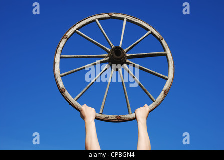 Mains tenant une vieille roue en bois contre le ciel bleu Banque D'Images