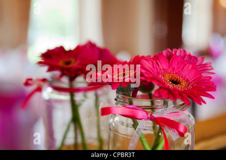 Gerberas rose dans un vase, un pot de confiture en verre. Réfléchi dans un miroir Banque D'Images