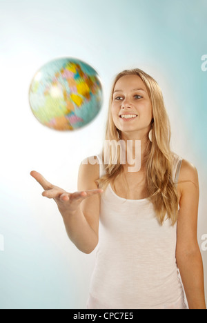 Belle jeune femme aux cheveux blonds jongle avec un globe. Banque D'Images