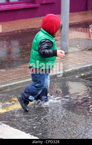 Jeune garçon éclaboussant par flaques dans une douche de pluie au Royaume-Uni Banque D'Images