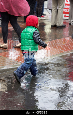 Jeune garçon éclaboussant par flaques dans une douche de pluie au Royaume-Uni Banque D'Images