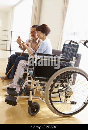 Couple à l'aide d'un smartphone sur un canapé et un fauteuil roulant Banque D'Images