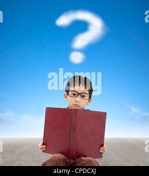 Little Boy holding book et fond de nuage de point d'interrogation Banque D'Images