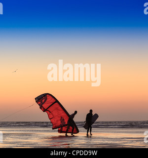 Deux hommes sur la plage au coucher du soleil à marcher avec un kite surfer naviguer, Essaouira, Maroc Banque D'Images