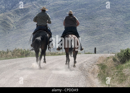 Cowboy et cowgirl cheval chevaux galopant dans une reconstitution du pony express sur un sentier de montagne. Banque D'Images