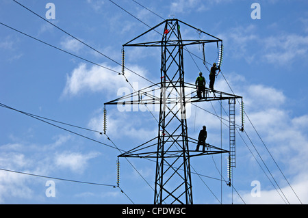 Les ingénieurs qui travaillent sur l'alimentation haute tension sont les lignes-silhouetté contre le ciel près du sommet d'un pylône, Perthshire, Écosse, Royaume-Uni Banque D'Images