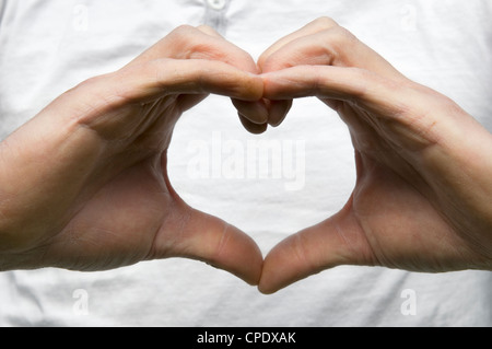 Homme de race blanche mains formant forme de coeur contre blanc T-shirt montrant concept de l'amour ou s'occuper de votre coeur ou corps Banque D'Images