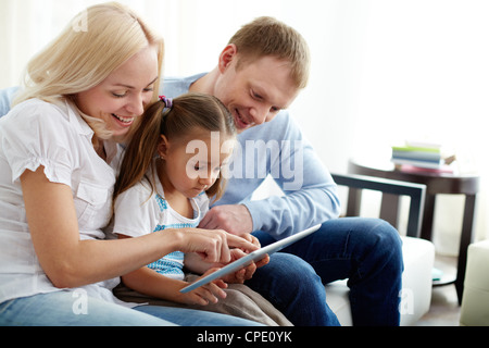 Portrait de parents heureux avec leur fille sitting on sofa with digital tablet Banque D'Images