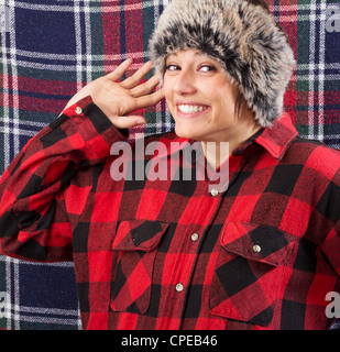 Souriante jeune femme portant chemise bûcheron et fur hat posing et forme avec sa main à l'appareil photo. Funny studio shot Banque D'Images