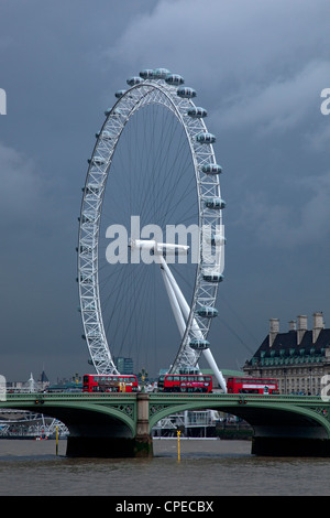 London Eye, grande roue du millénaire avec des bus rouge et le pont de Westminster contre dark storm sky, Londres, Angleterre. Banque D'Images