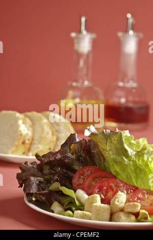 Une salade de laitue avec des tranches de pain au levain et une salière d'huile et de vinaigre sur un fond de couleur rose. Banque D'Images