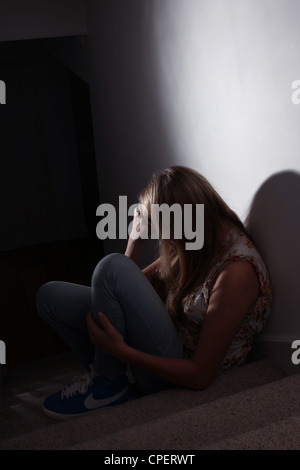 Jeune fille assise sur un escalier sombre vue arrière Banque D'Images