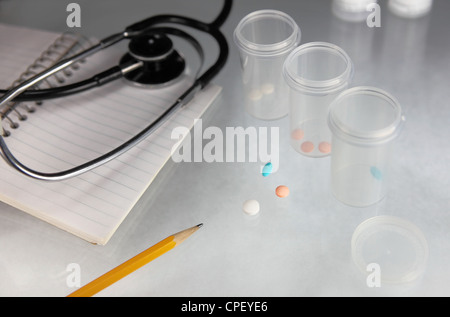 Comprimés de différentes couleurs, les contenants en plastique, un ordinateur portable, d'un crayon et d'un stéthoscope sur une table en verre Banque D'Images