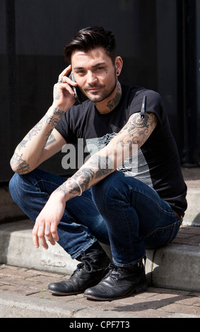Portrait d'un jeune homme assis à la mode et de parler sur un téléphone cellulaire mobile, Spitalfields, Londres, Angleterre, Royaume-Uni Banque D'Images