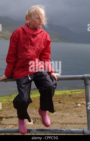 Jeune fille portant un anorak rouge assis en plein air sur une balustrade Banque D'Images
